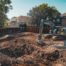 A professional, cinematic wide shot of a neatly executed pool removal site in a sunny Oklahoma City backyard. In the foreground, the hole where the pool used to be is perfectly filled, compacted, and leveled with clean topsoil. In the middle ground, a clean, modern excavator with the F5 Demolition logo is actively compacting the final layer of fill. The image should convey precision, completion, and the reclamation of space, with an Oklahoma-style residential home visible in the background. High-contrast, vibrant, and professional photography style.