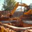 A high-resolution, realistic wide shot of a professional yellow excavator carefully removing a concrete swimming pool in a suburban Oklahoma City backyard. Bright sunny day, red dirt visible, professional crew in high-visibility vests nearby. Cinematic lighting, 8k resolution